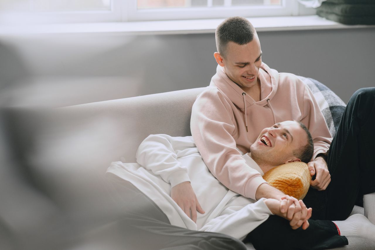 Man in a pink hoodie laughing with his partner on a sofa