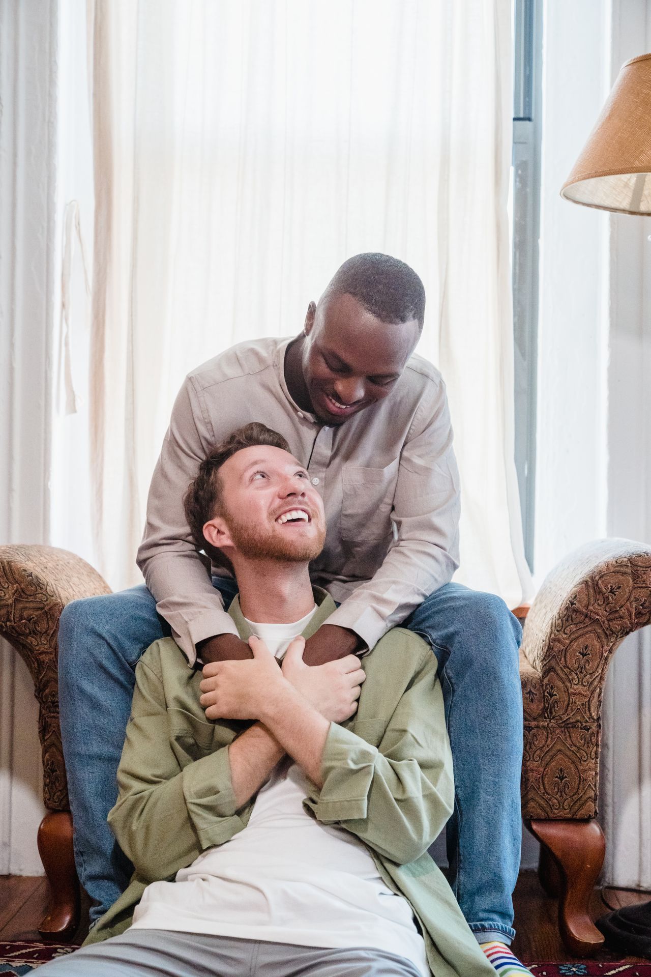 Man hugging his laughing partner from behind as he sits in an armchair
