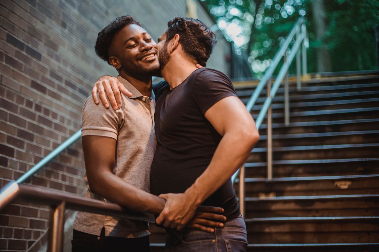 Man kissing his partner on the cheek on an outdoor staircase