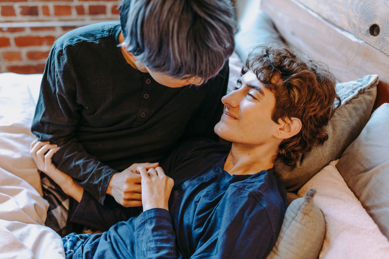 Two young men cuddling and smiling on a bed