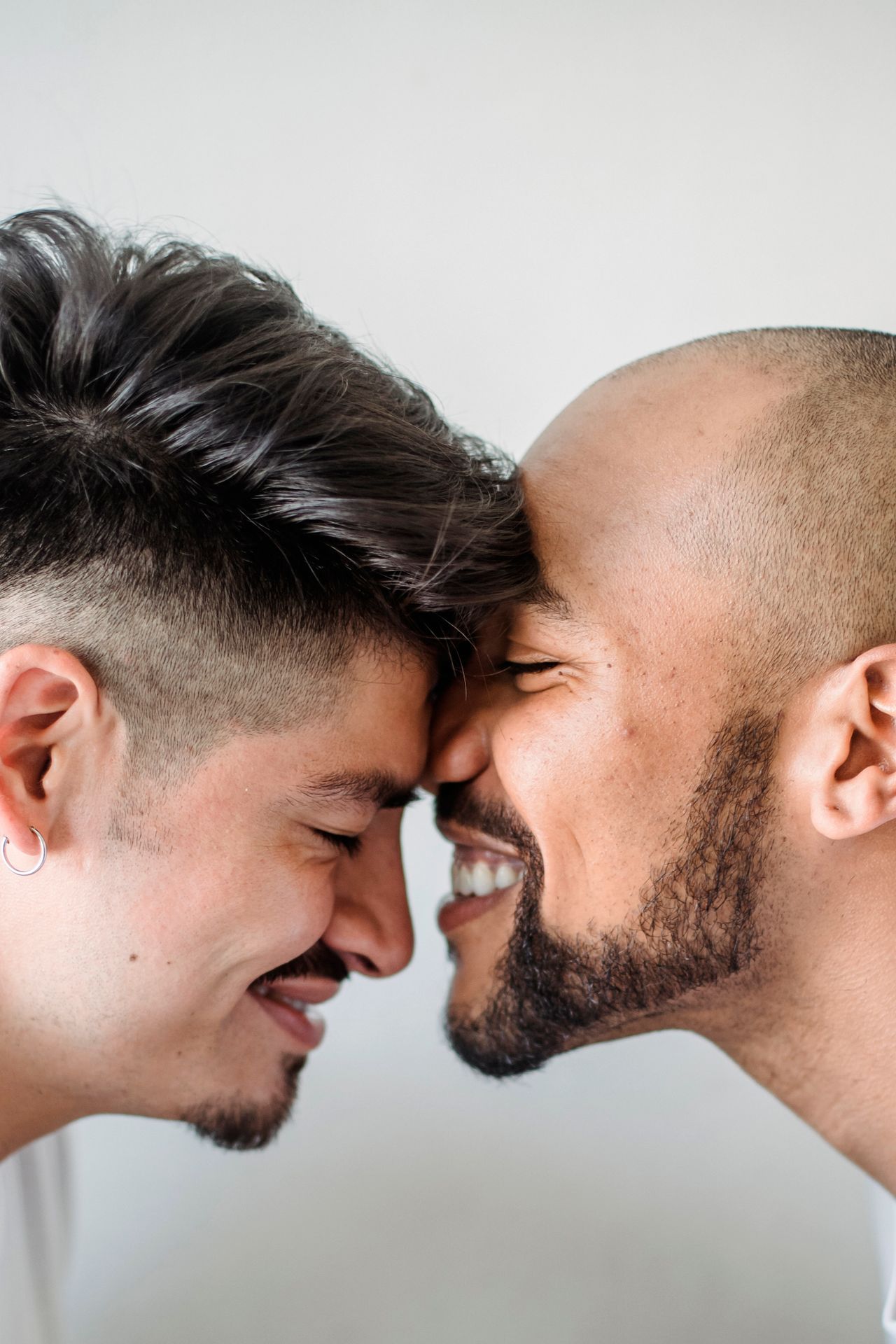 Two smiling men touching foreheads against a light background