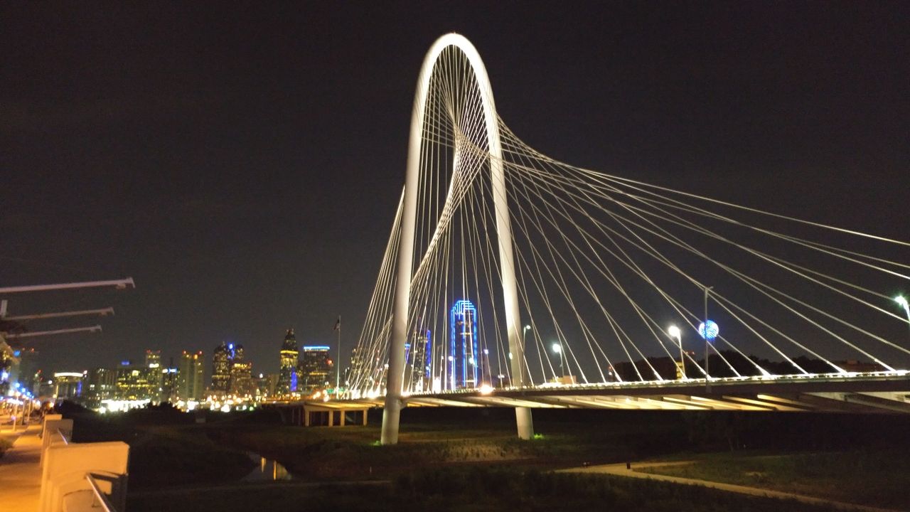 Margaret Hunt Hill Bridge lit up at night with the Dallas skyline behind it