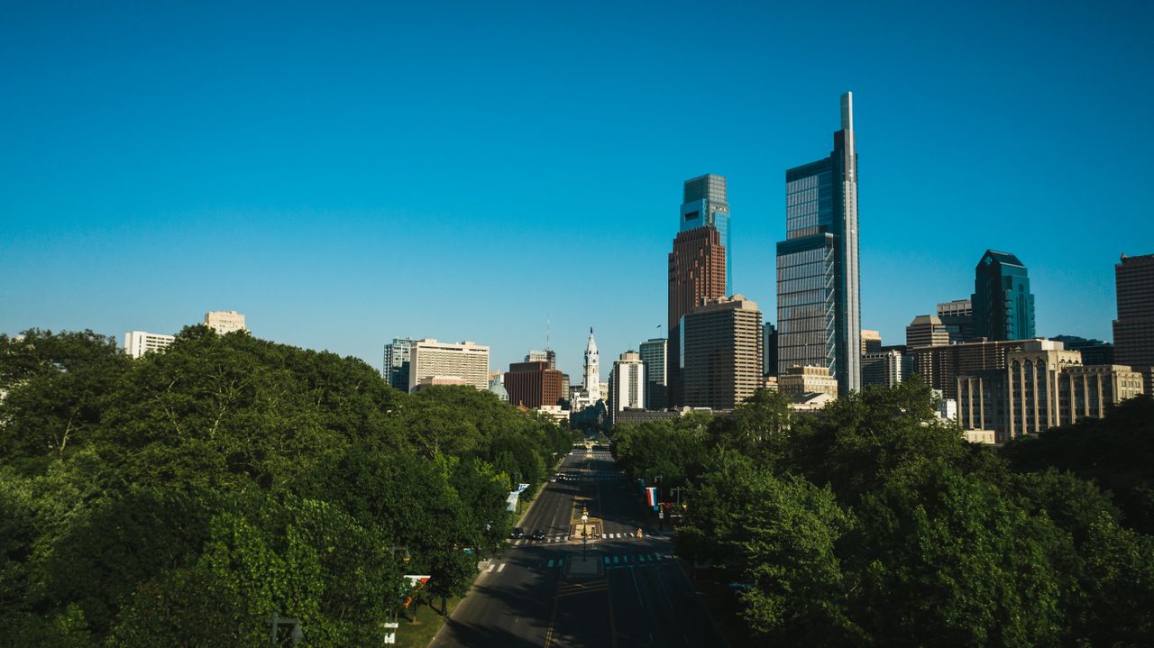 Philadelphia skyline rising above green trees under a blue sky