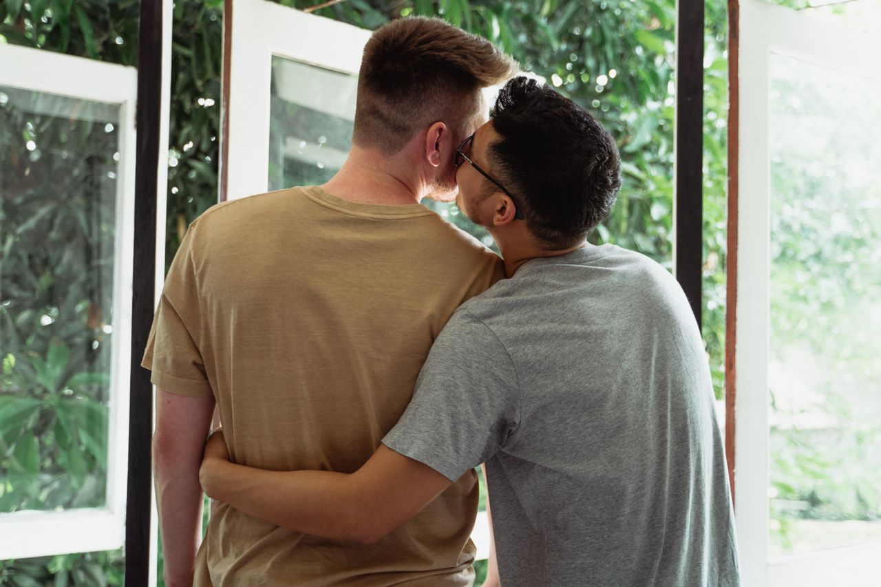 Man kissing his partner's cheek on a sunny balcony