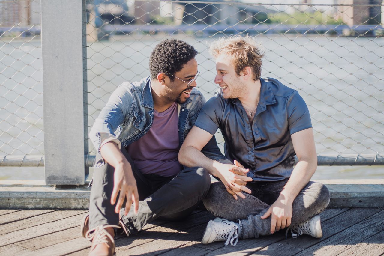 Two men sitting on a wooden deck and smiling at each other