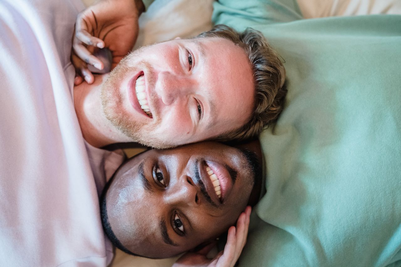 Two smiling men lying face to face on colorful pillows
