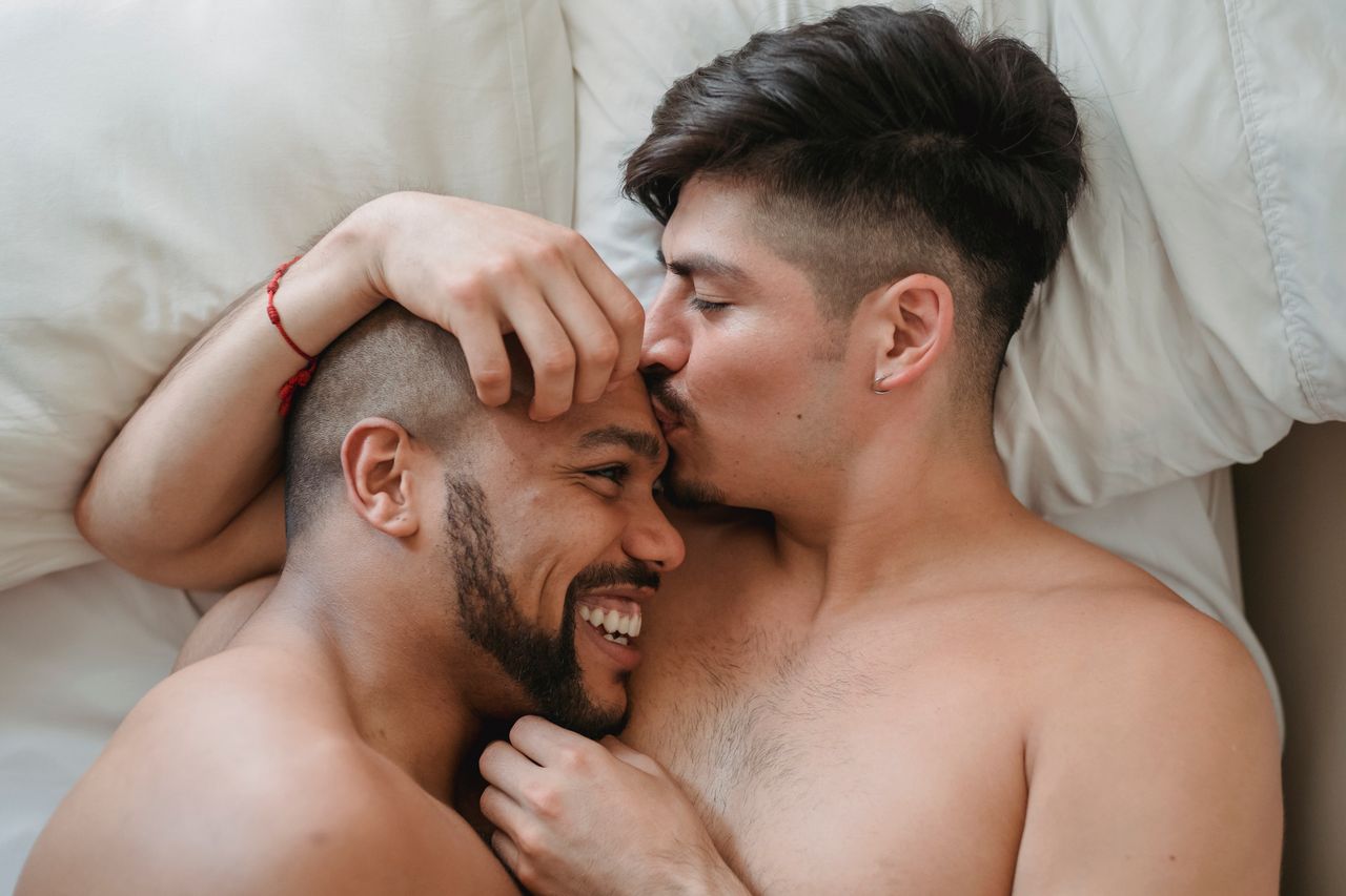 Man kissing his partner's forehead as they lie in bed