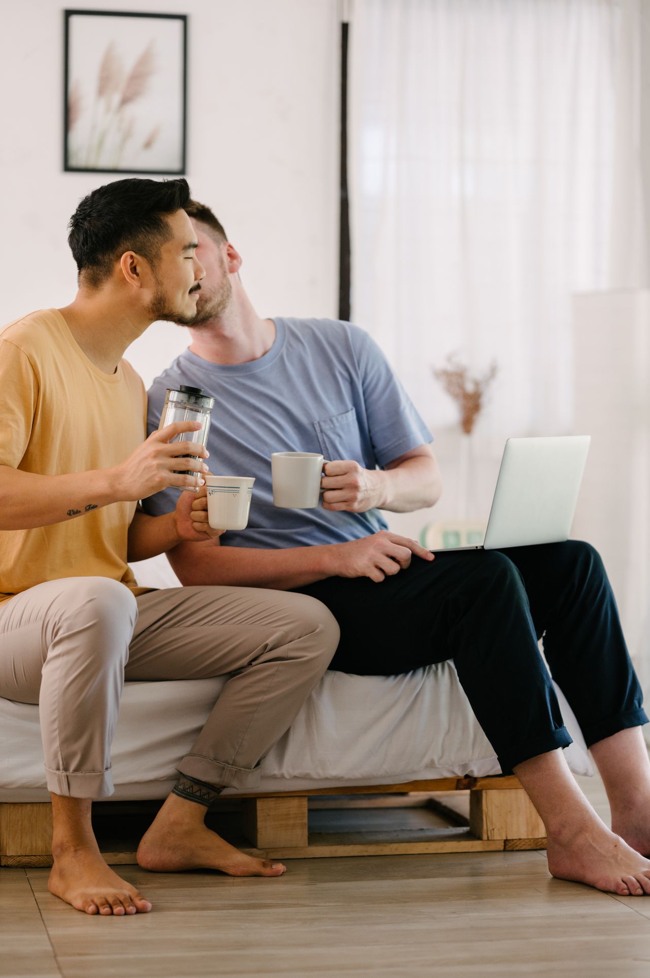 Two men sharing coffee and a kiss on a sofa
