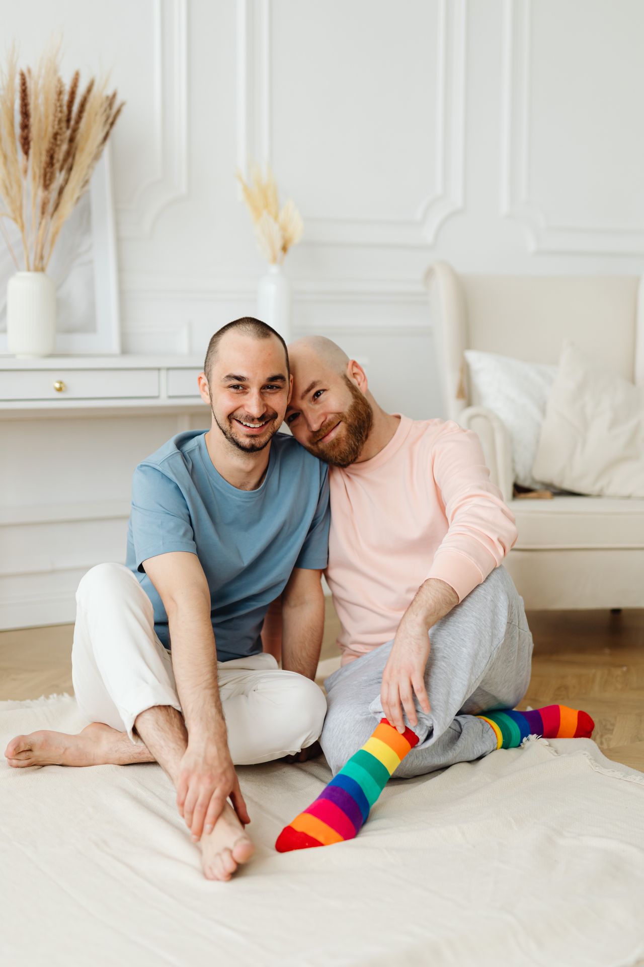 Two men in rainbow socks sitting close together on a white rug
