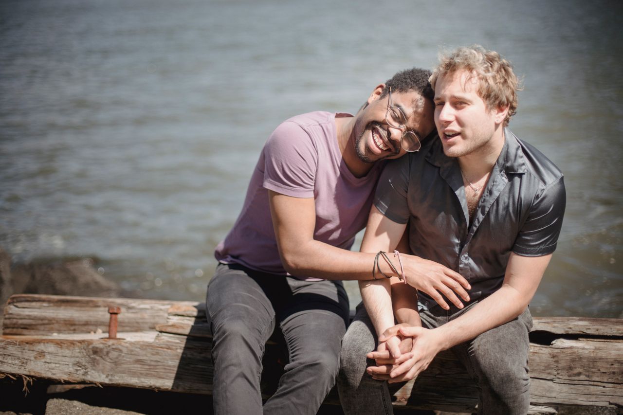 Two men laughing together on a wooden bench by the water