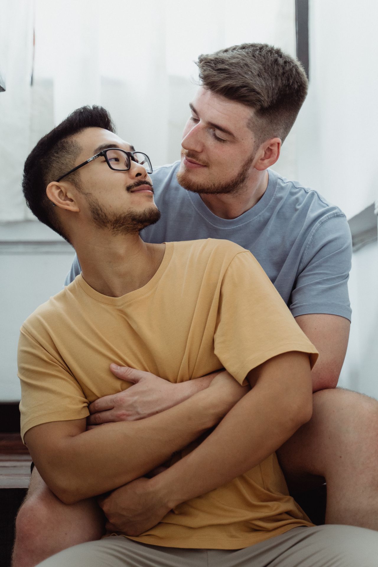 Man in glasses smiling as his partner hugs him from behind