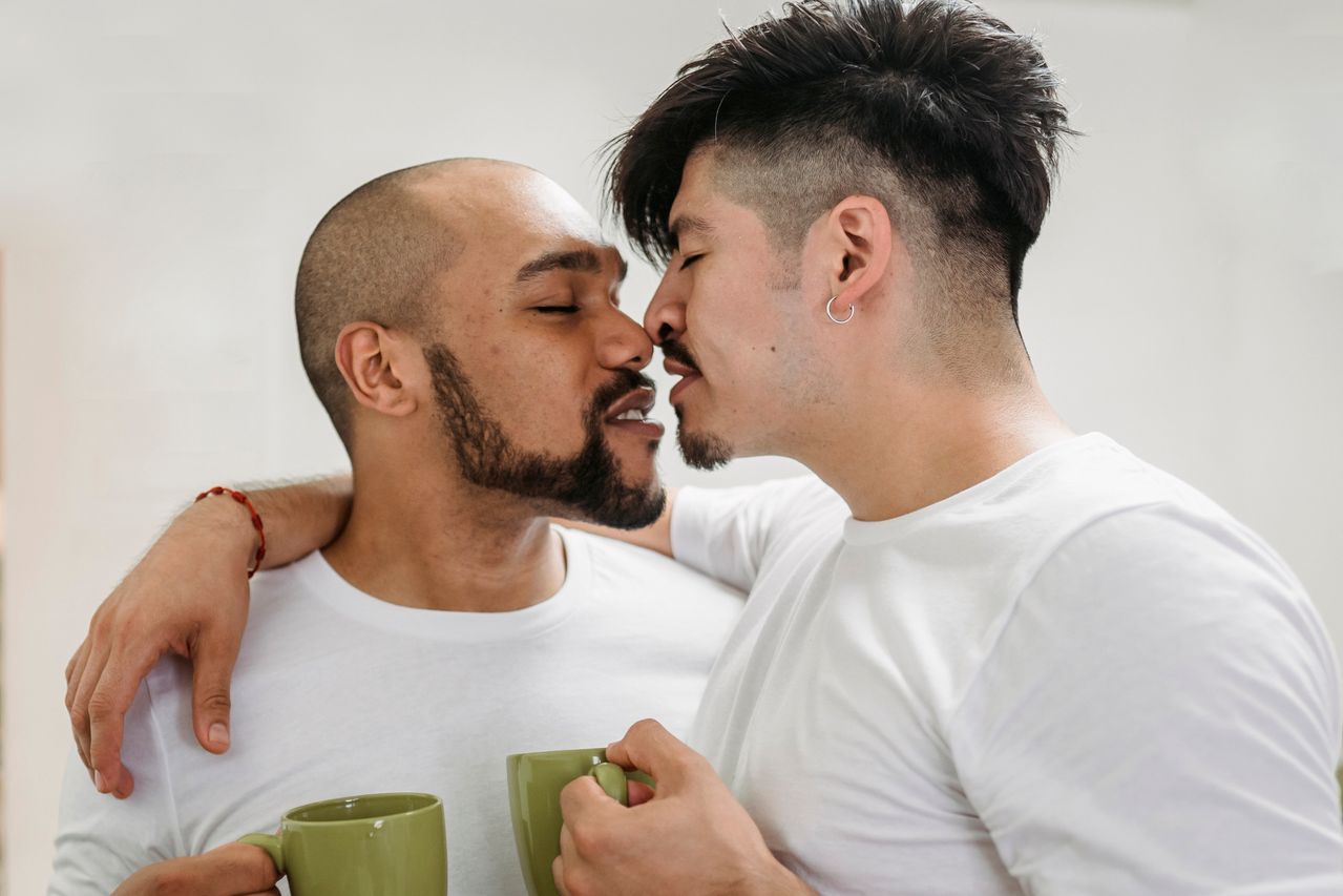 Two men kissing while holding coffee mugs