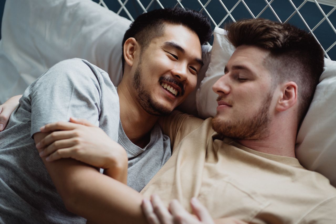 Two smiling men lying close together on soft pillows