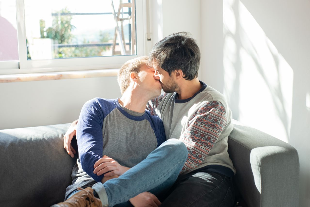 Two men kissing on a sofa by a sunny window