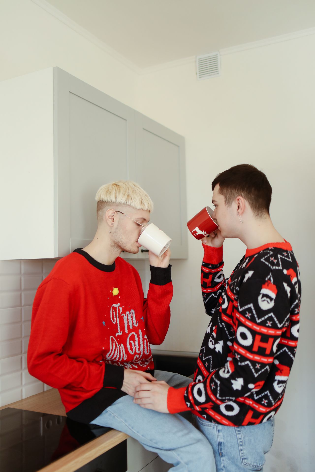 Two men in festive sweaters drinking coffee in a kitchen