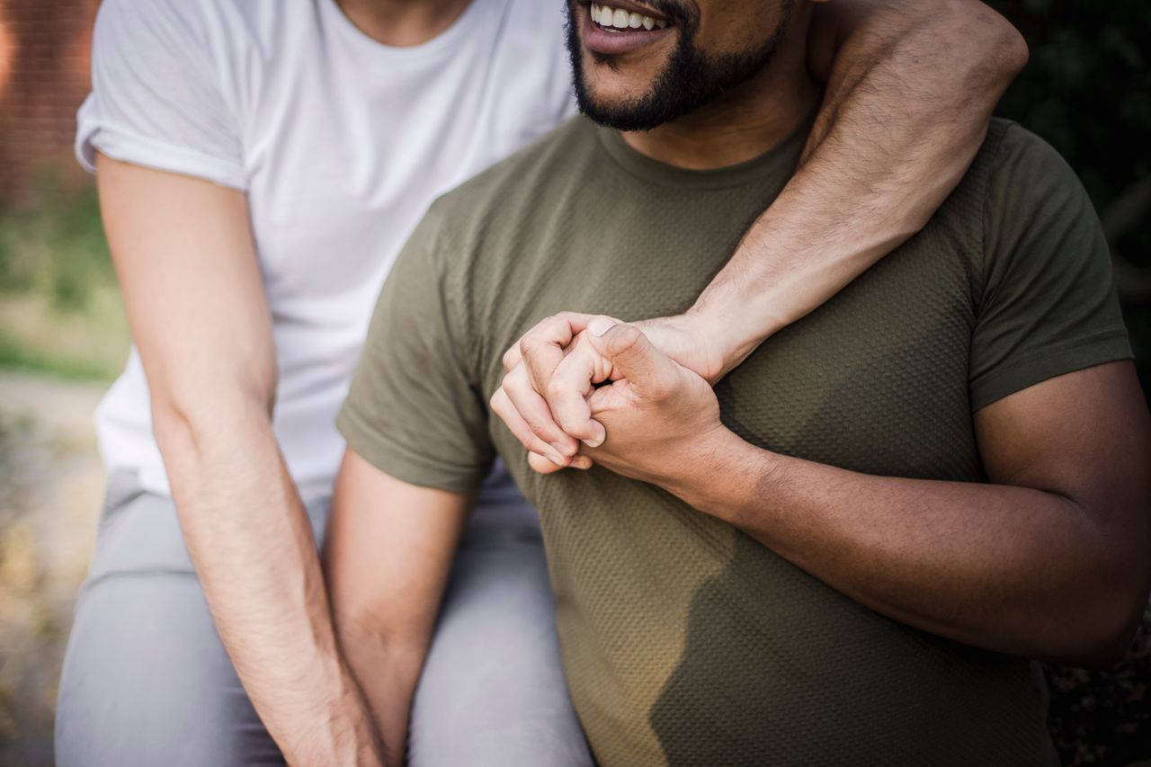 Man with his arm around his partner, holding his hand