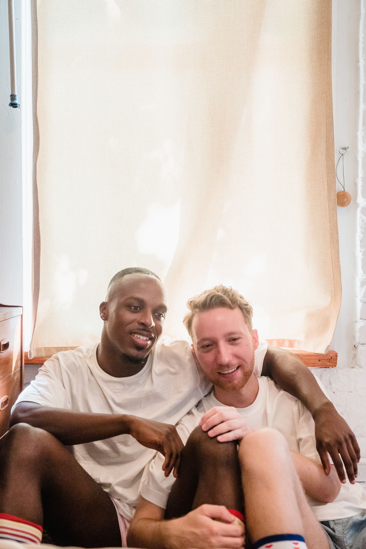 Two smiling men sitting close together on a windowsill