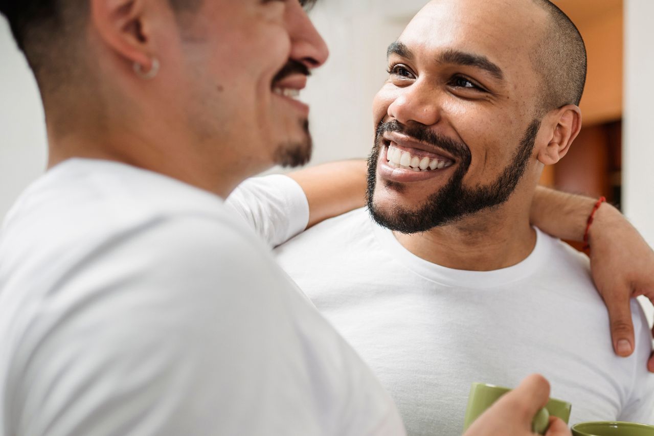Two smiling men sharing a coffee at home