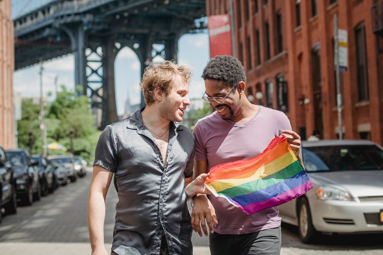 Two men walking down a city street holding a rainbow flag