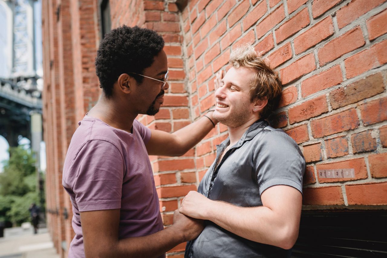 Man touching his partner's face as they stand by a brick wall