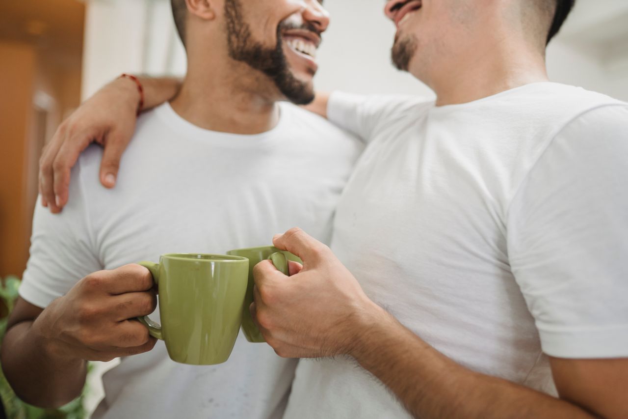 Two men in white T-shirts holding green coffee mugs and smiling