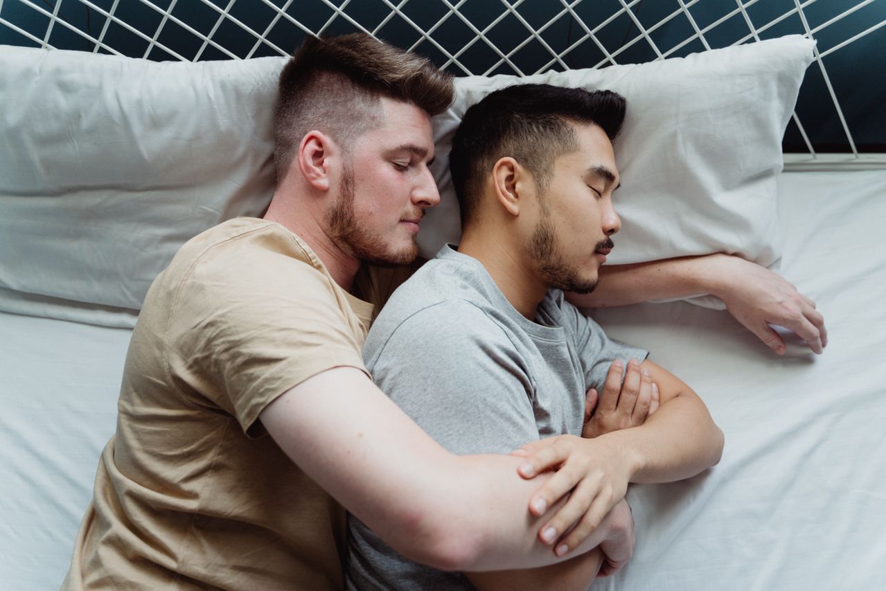 Two men cuddling on white pillows in bed
