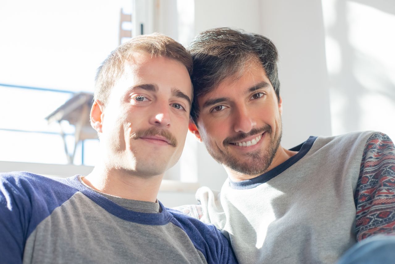 Two smiling men taking a selfie together at home