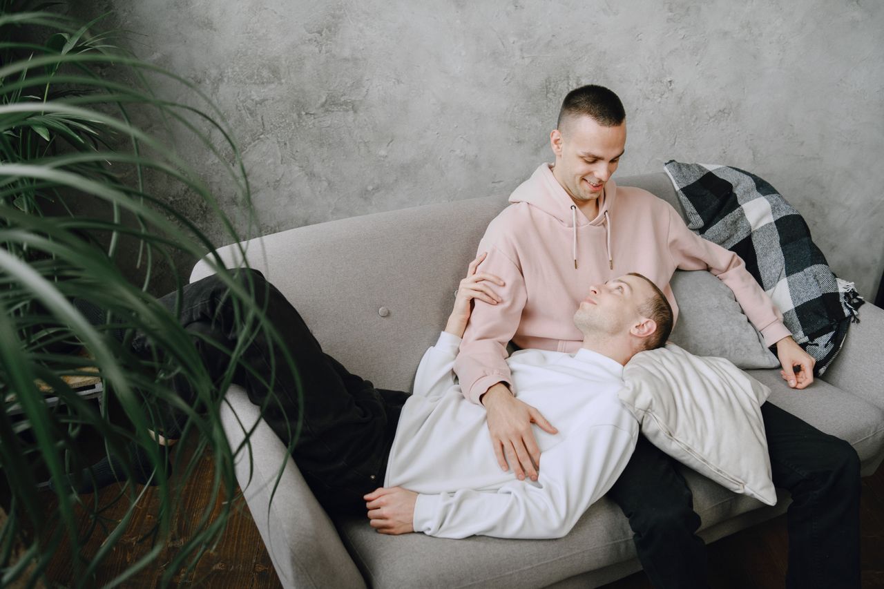 Man in a pink shirt hugging his partner on a sofa