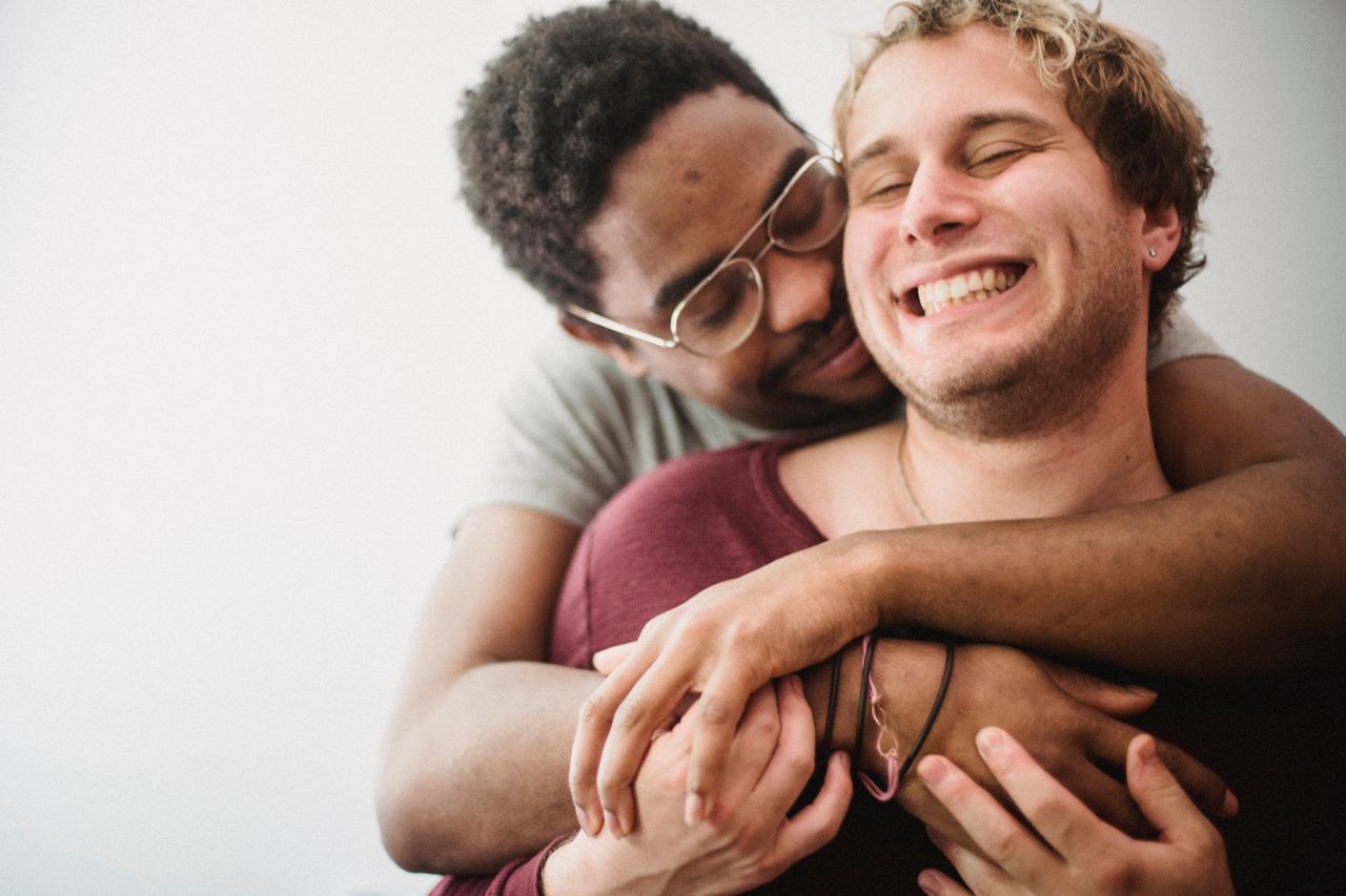 Man in glasses hugging his laughing partner from behind