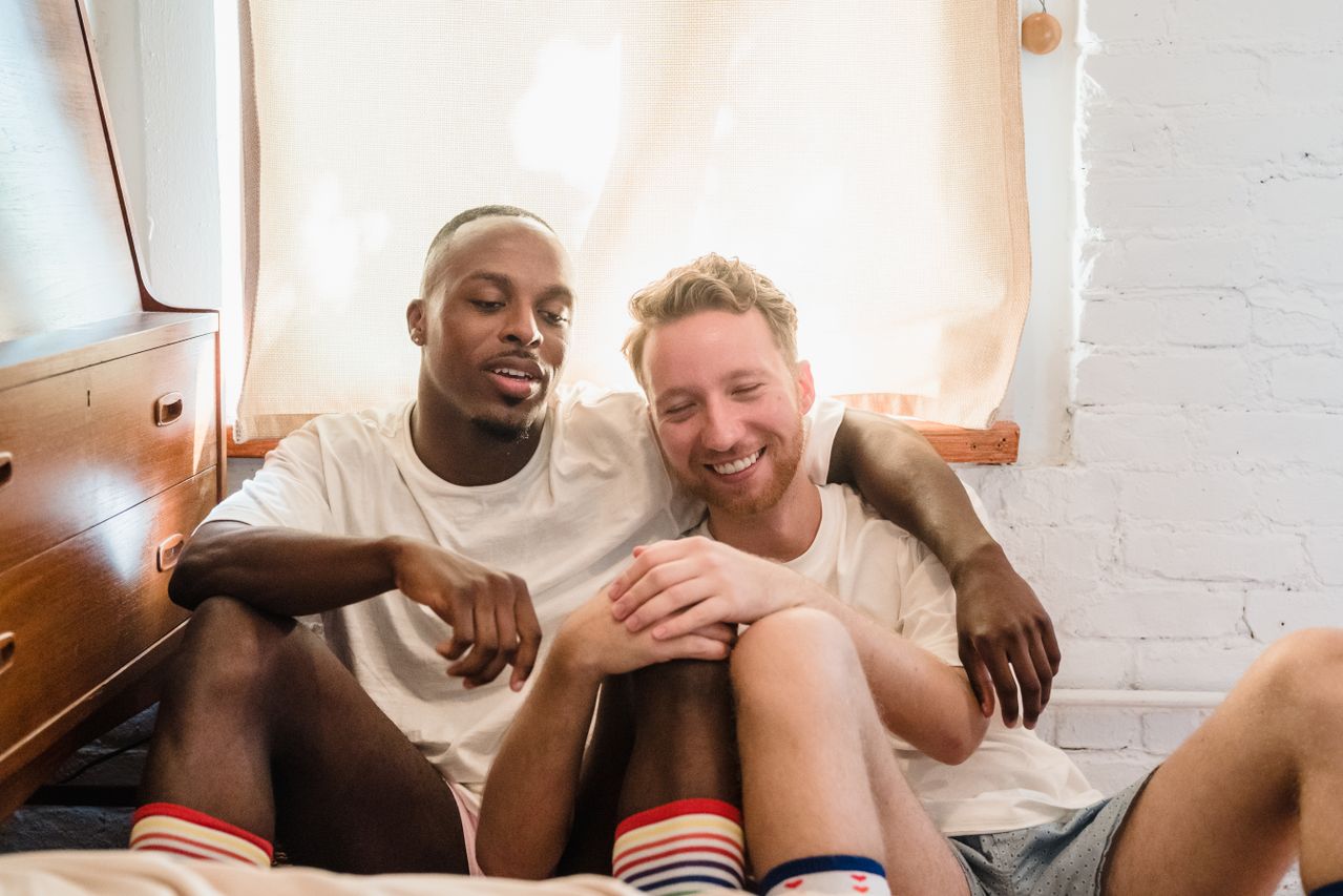 Two smiling men sitting together on a bed in colorful socks