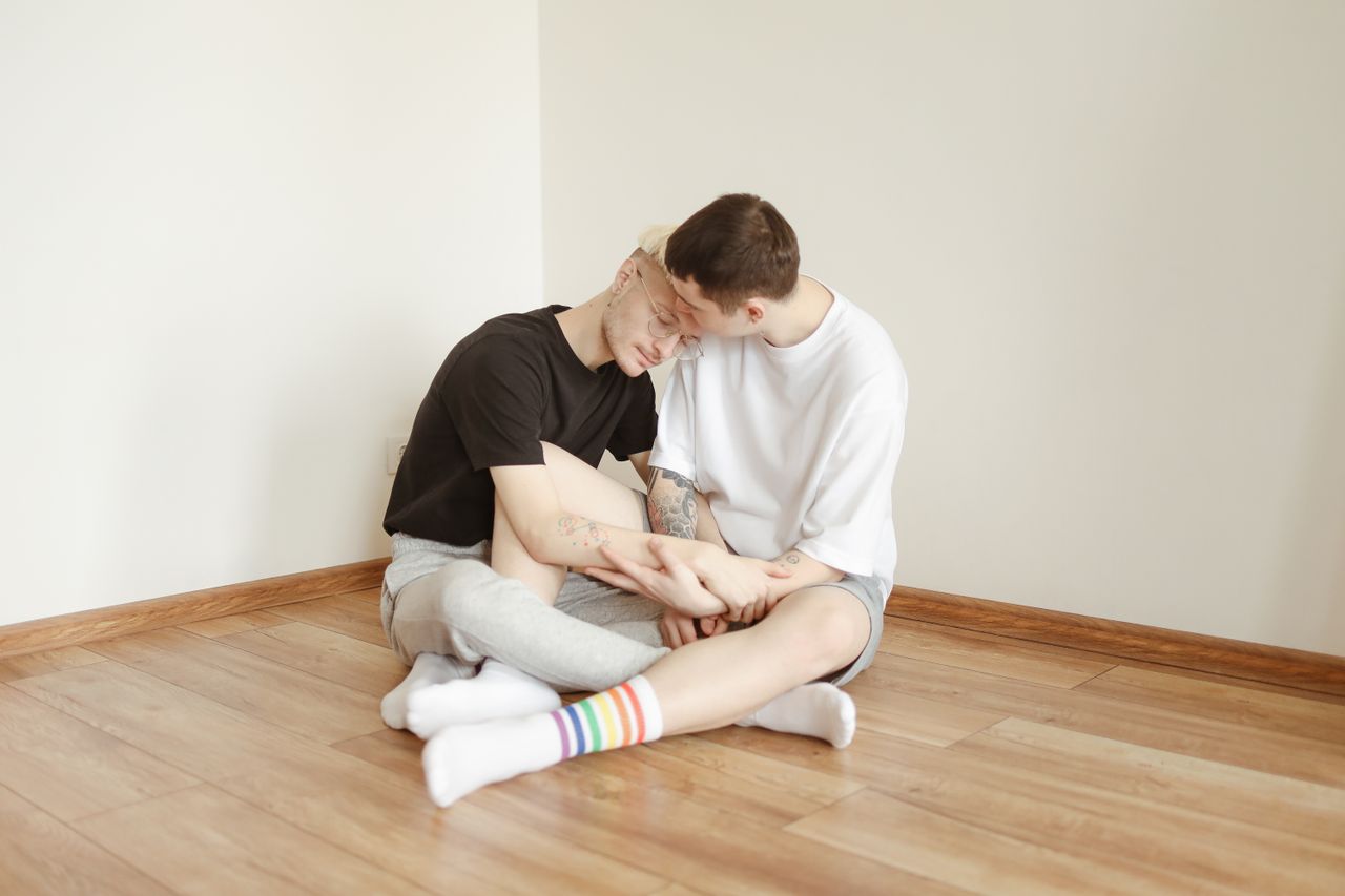 Two men sitting close together on a wooden floor