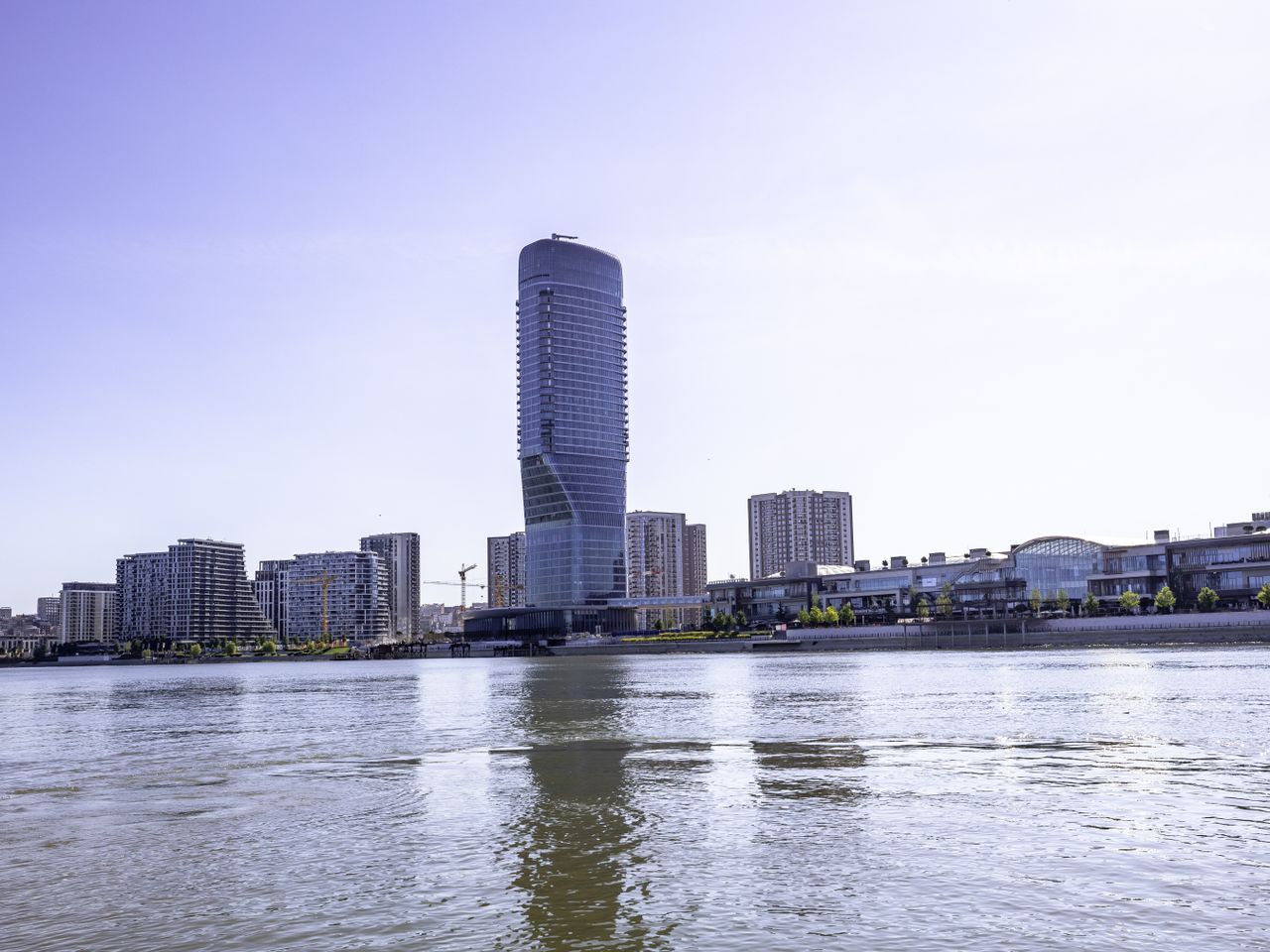 Tall cylindrical tower on a riverbank under a pale sky