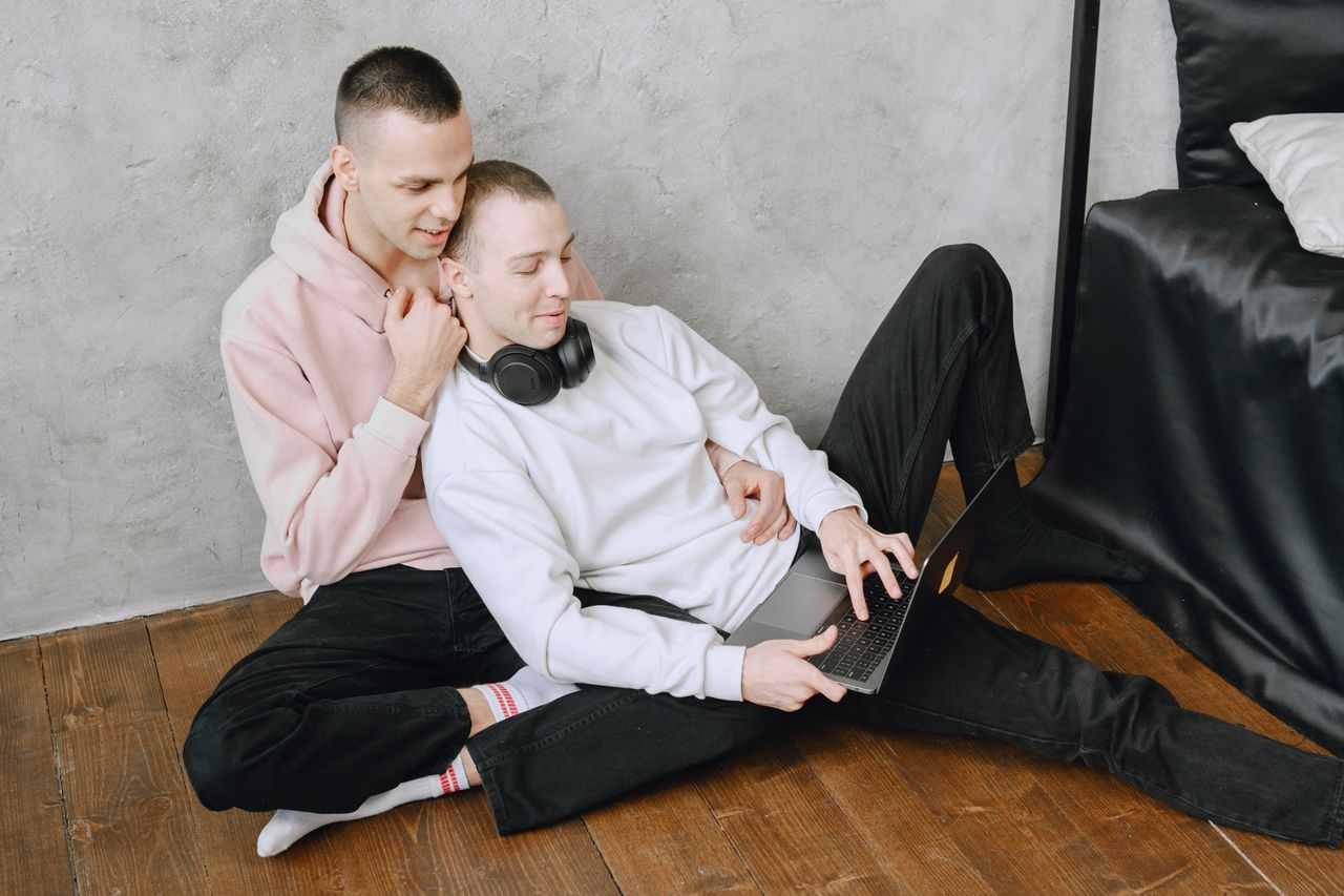 Man in a pink hoodie hugging his partner as they sit on the floor