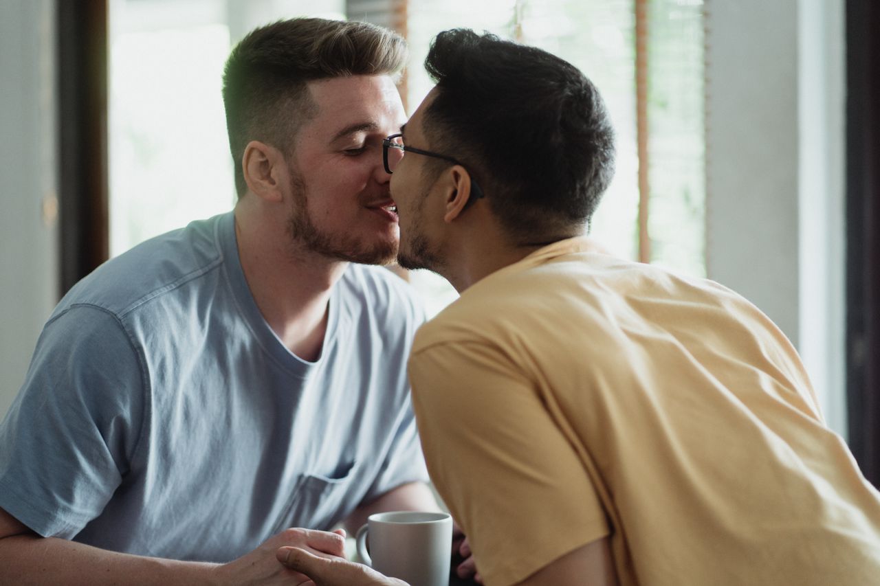 Two men kissing by a window with coffee cups