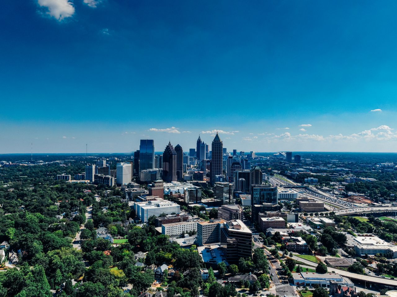Aerial view of the Atlanta skyline above green trees on a sunny day