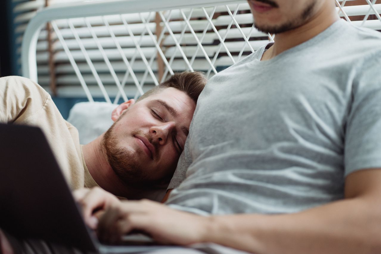 Man resting his head on his partner's shoulder while they relax with a laptop