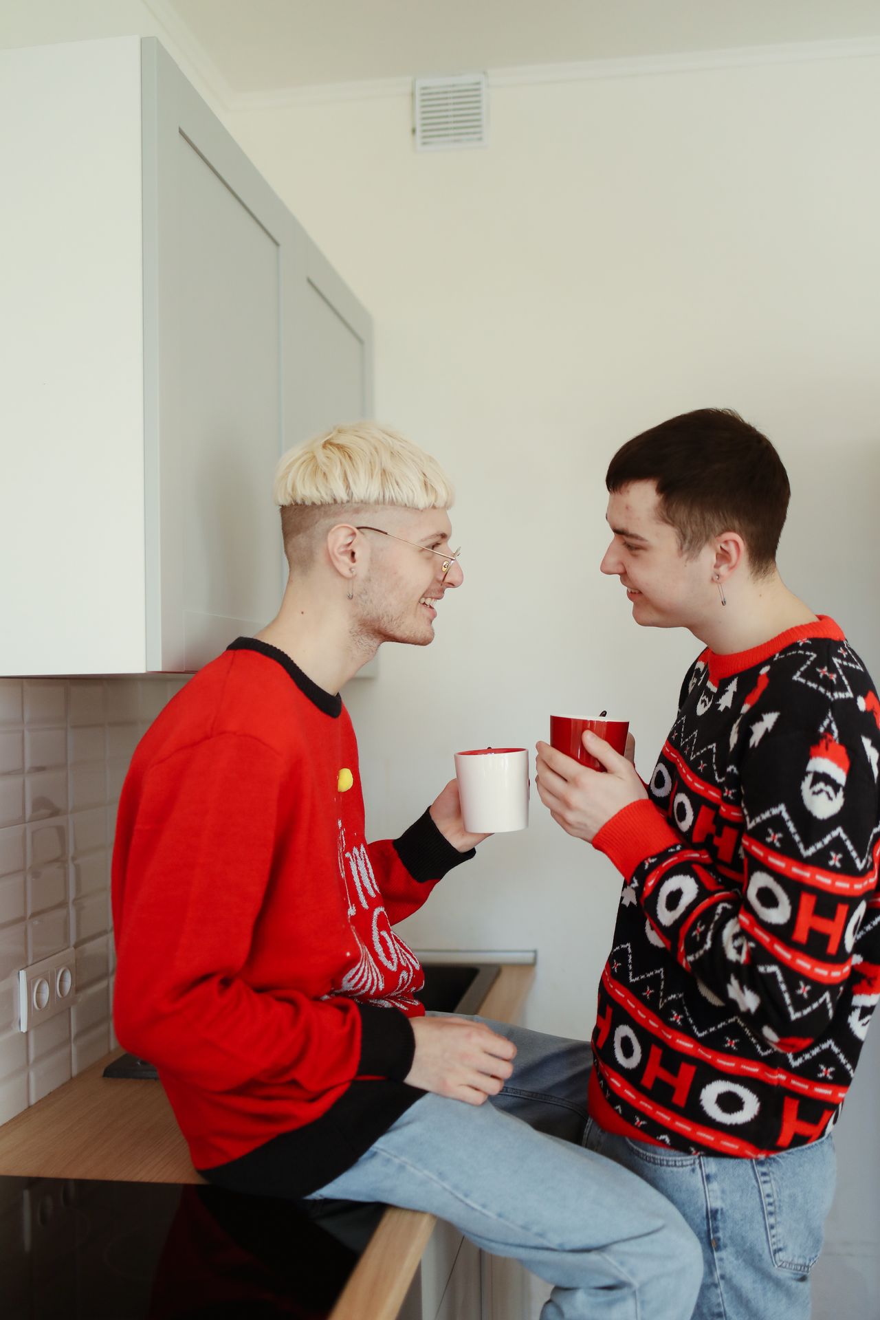 Two men in festive sweaters chatting over coffee in a kitchen