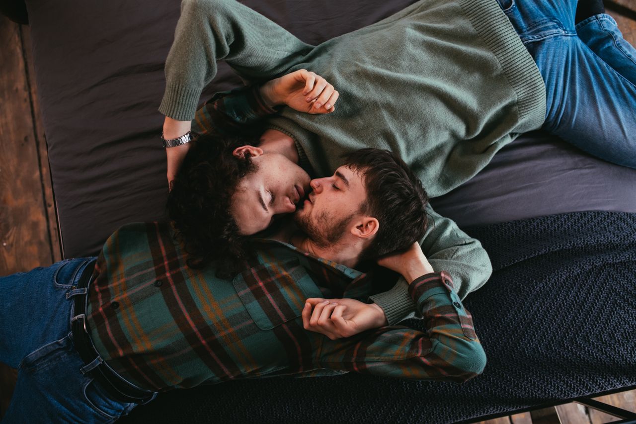 Two men lying head to head on a sofa about to kiss