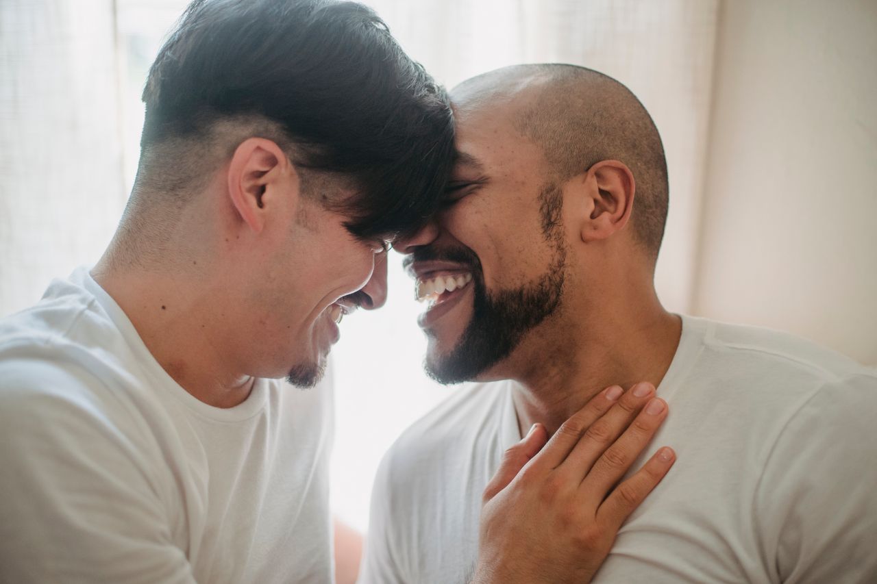 Two laughing men touching foreheads in a bright room