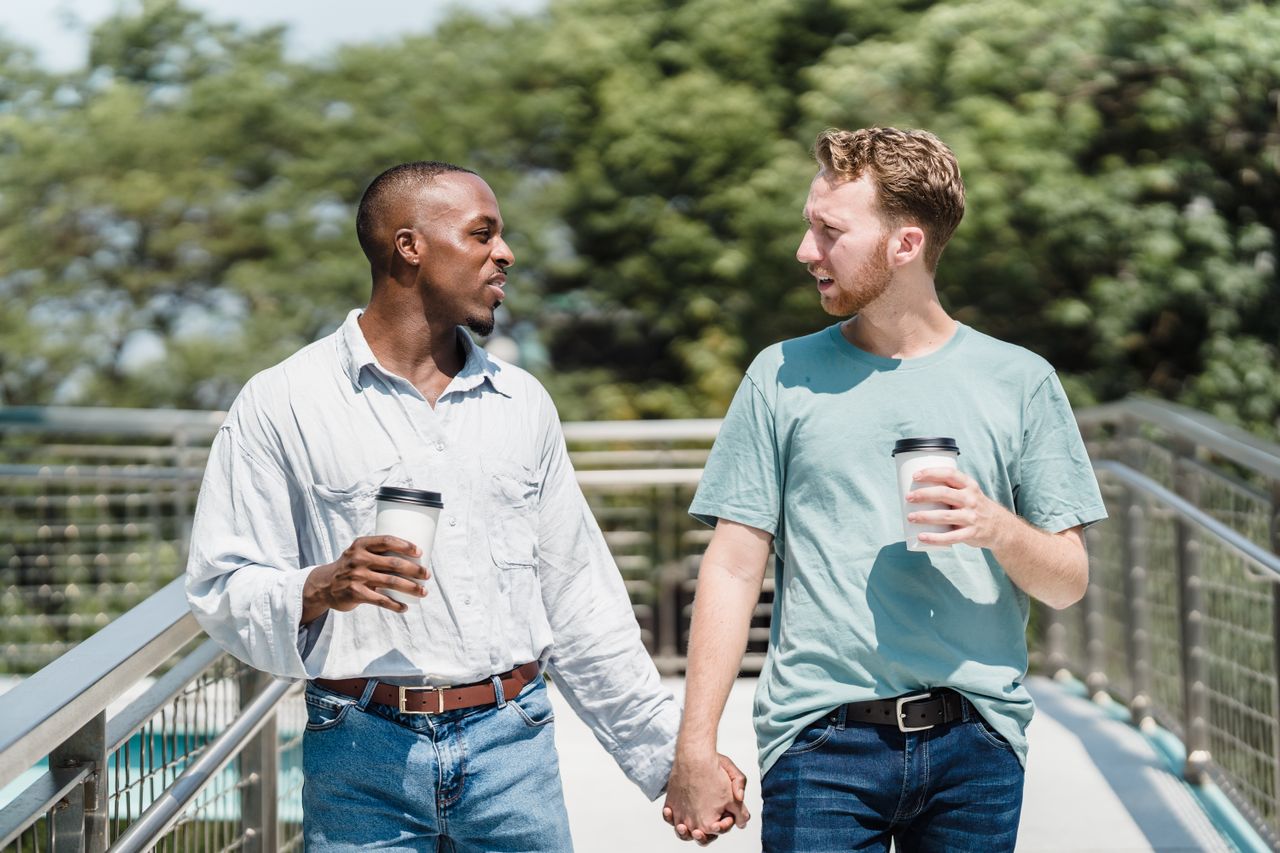 Two men holding hands and coffee cups as they walk down outdoor steps