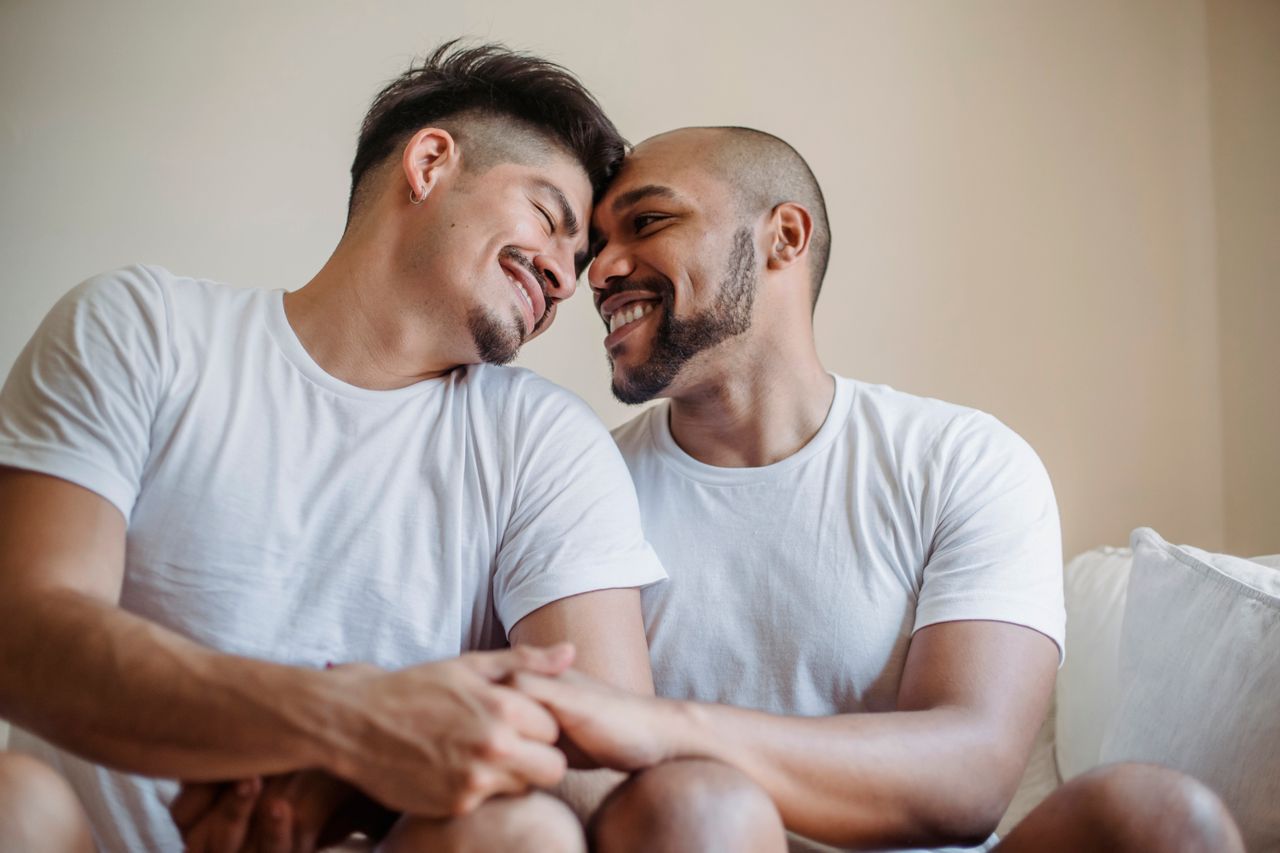 Two smiling men in white T-shirts touching foreheads and holding hands
