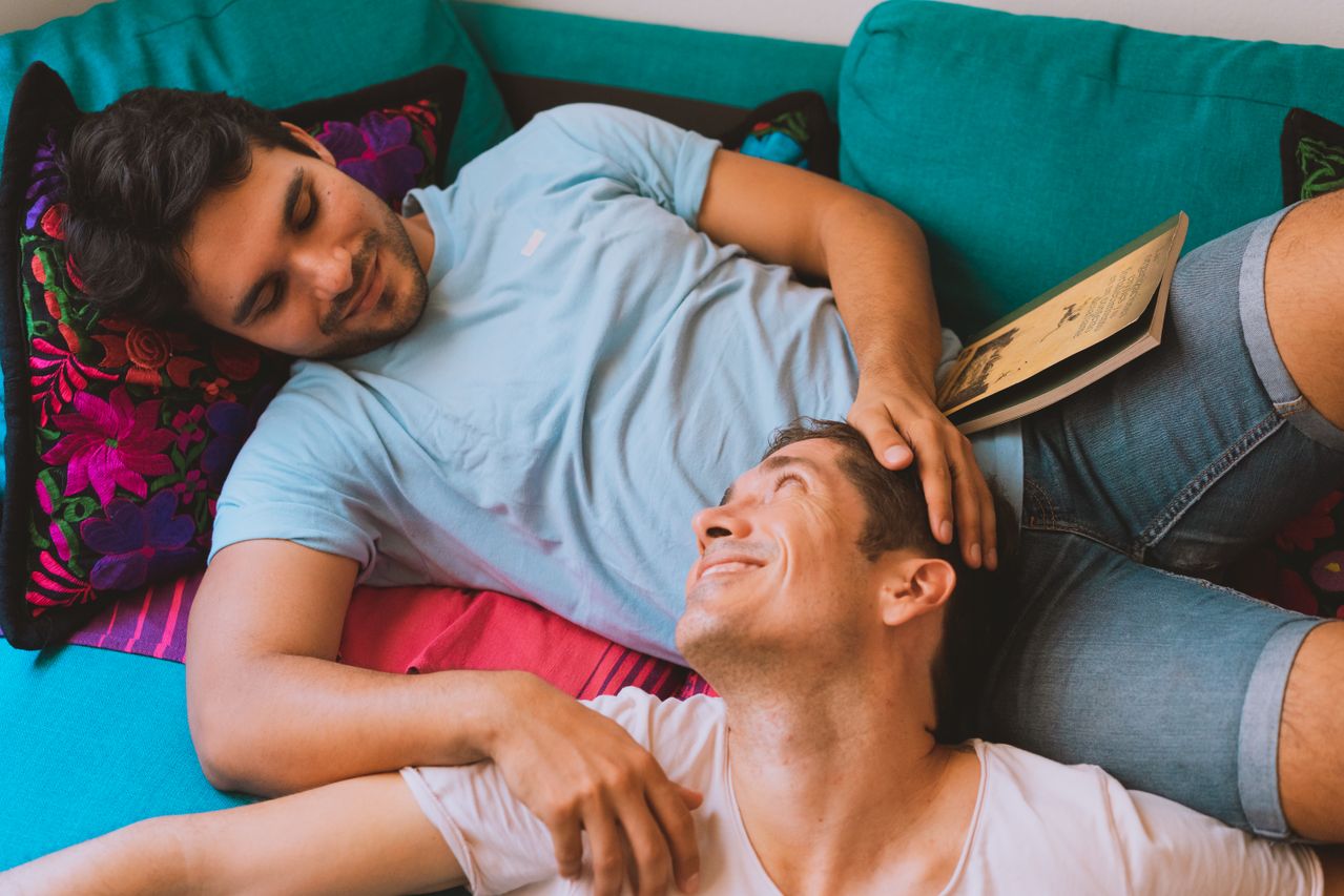 Man stroking his partner's hair as they relax on a colorful sofa