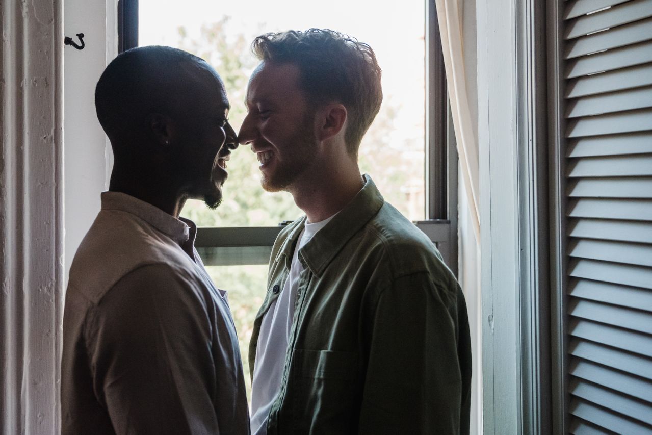 Two men smiling at each other by an open window