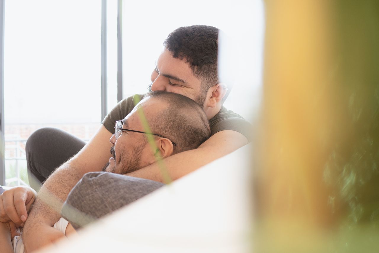 Man resting his head on his partner's back by a sunny window