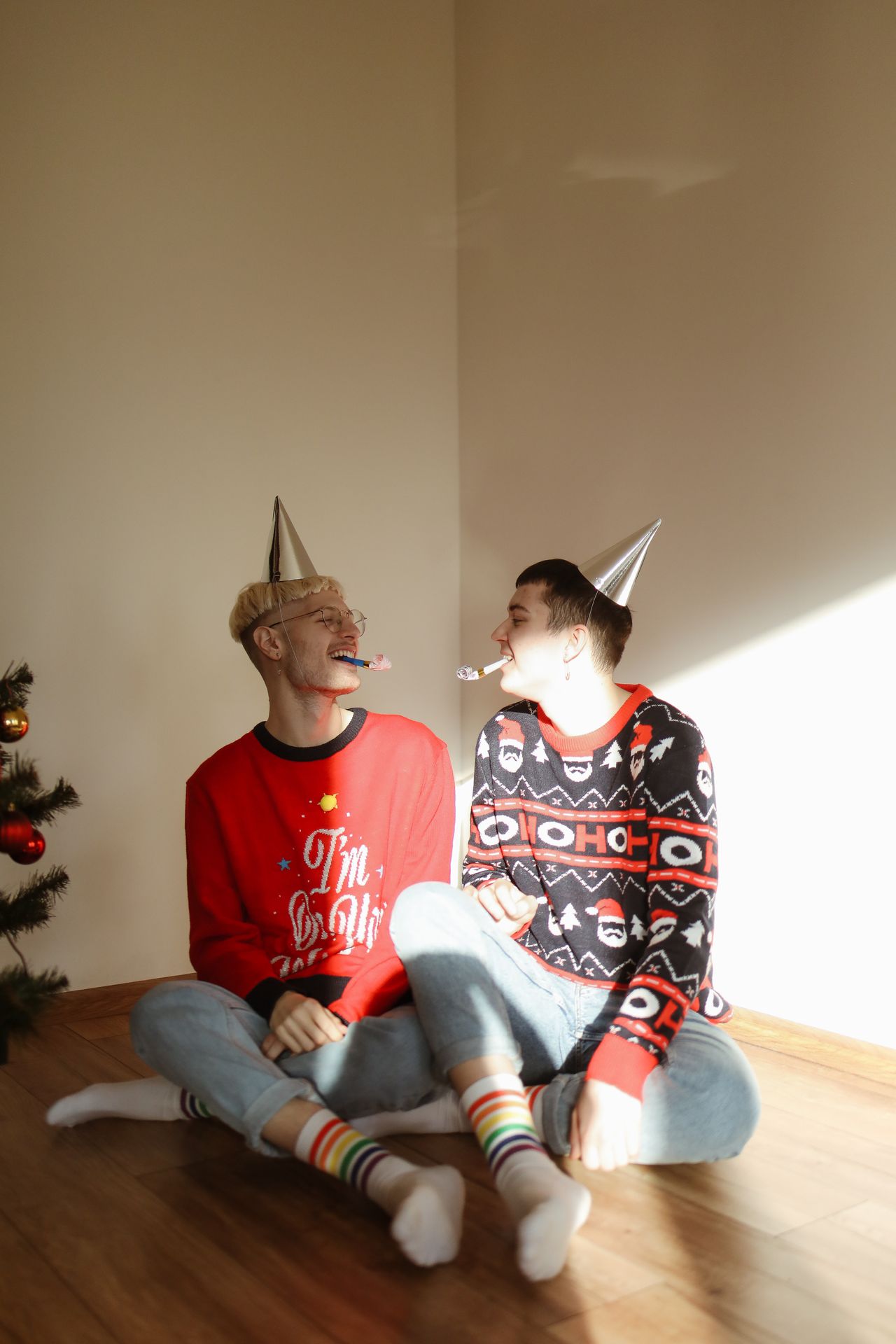 Two men in holiday sweaters and party hats sitting on the floor
