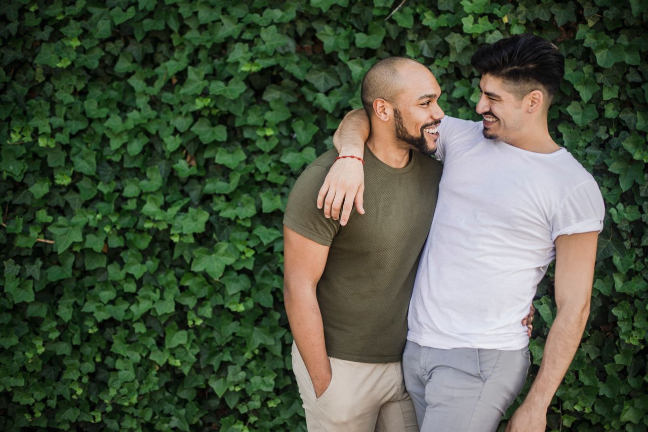 Two men with arms around each other laughing in front of an ivy wall