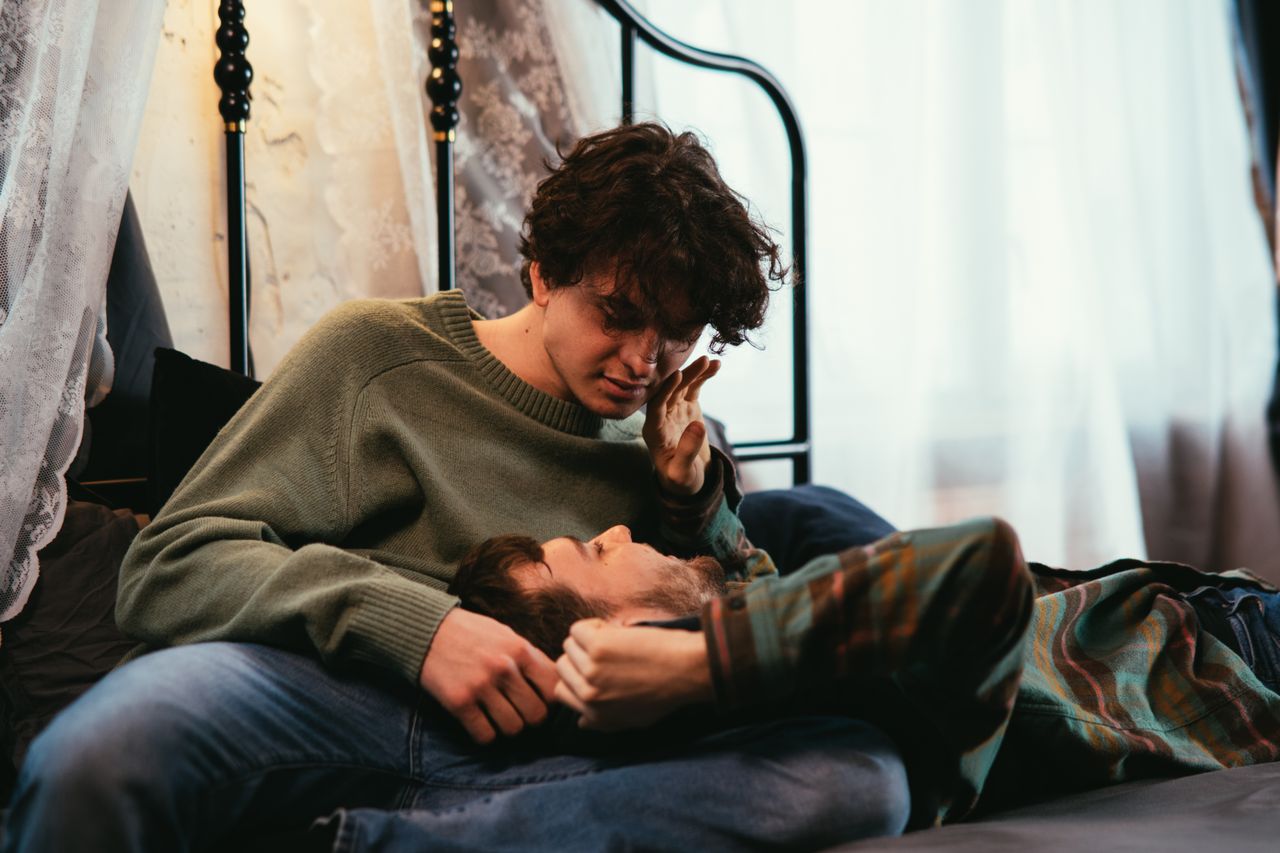 Man resting his head in his partner's lap on a sofa by the window