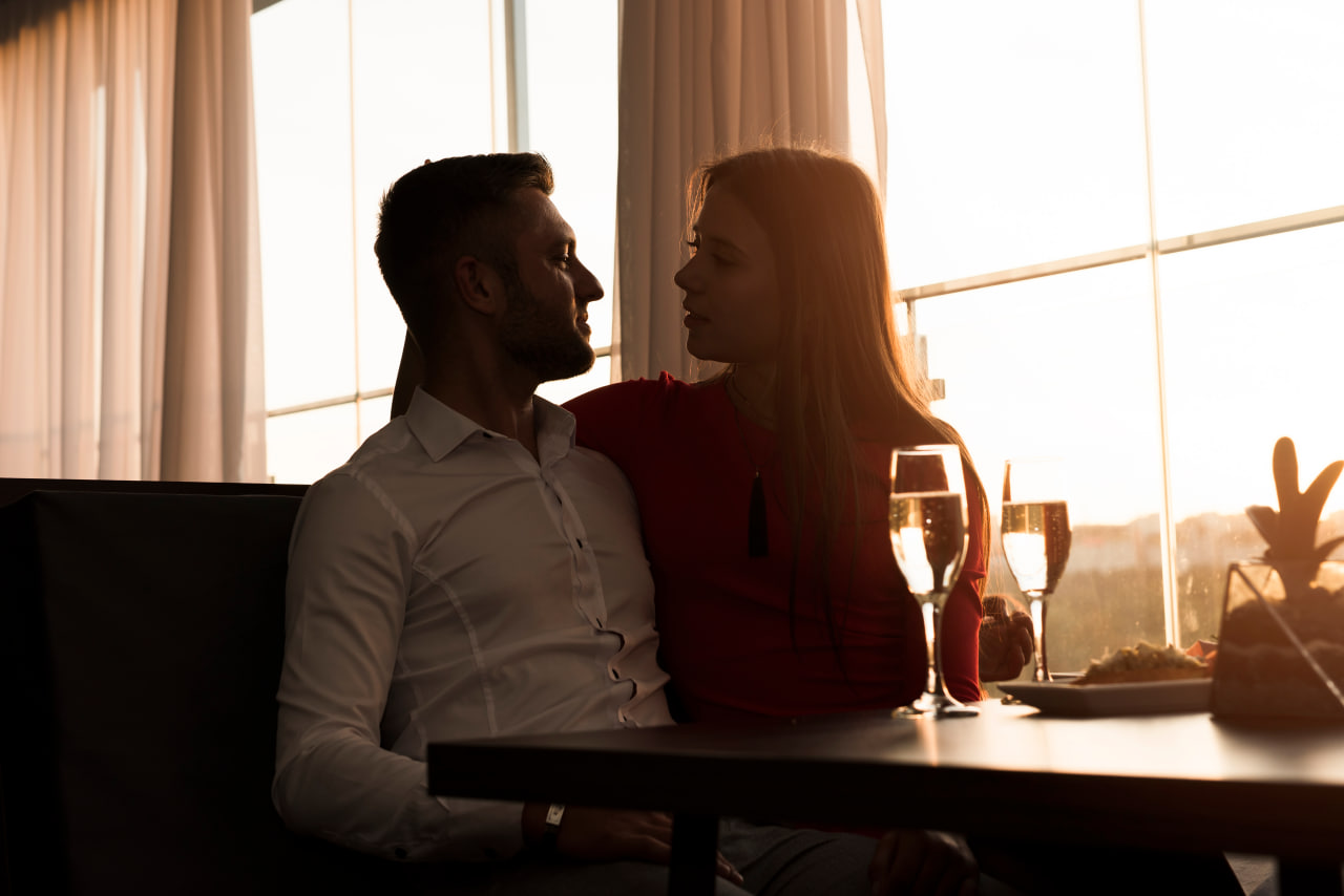 A sophisticated couple enjoying a romantic sunset dinner with champagne, representing a successful connection found through a top dating app for millionaires like Kismia.