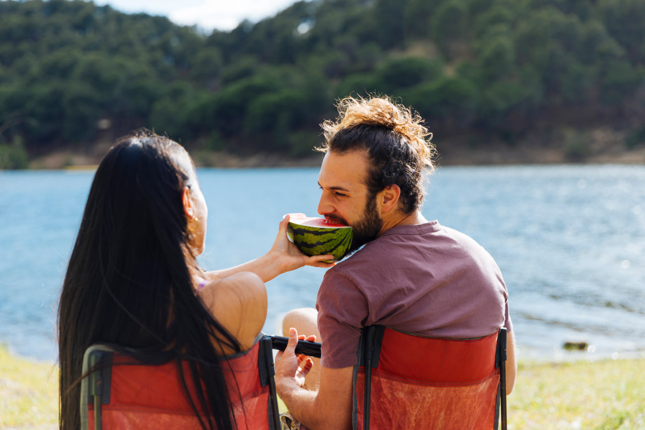 Happy couple sitting by the lake eating watermelon, a great match from a colombian dating site.